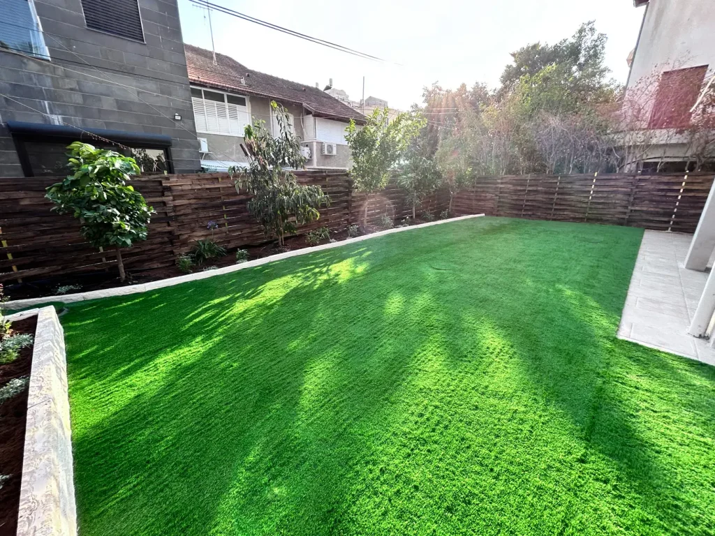 Completed garden renovation in Rehovot with synthetic grass, privacy fencing, stone planting beds and new trees